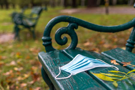 Used disposable face mask on bench in park. Environmental damage and pollution during coronavirus covid-19 pandemic in city. New Norman in town at autumnの写真素材