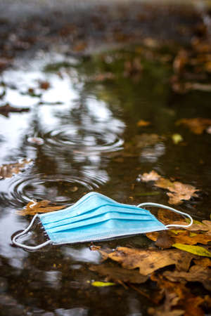 Used face mask in puddle on street. Pollution problems during covid-19 pandemic. New normal in cityの写真素材