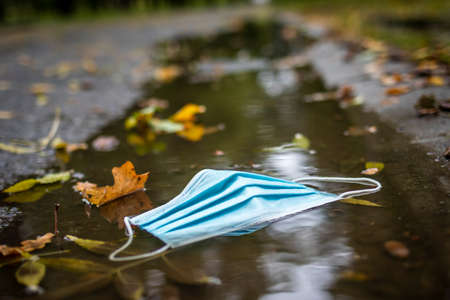 Disposable face mask in puddle on street. Environmental damage and pollution during coronavirus covid-19 pandemic in cityの写真素材