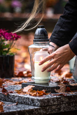 Woman is putting candle lantern at grave in cemetery. Grief for dead person. Closeup of female hands...