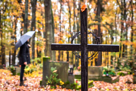 Religious cross in cemetery. Mourning woman in black standing next to tombstoneat graveyard in rain. Silent memory for dead relativesの写真素材