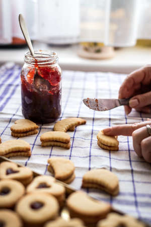 Cooking Linzer cookies. Hand preparing and filling baked pastry with jam. Traditional homemade Christmas sweetsの写真素材