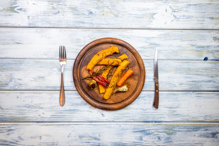 Roasted pumpkin slices and vegetable on wooden plate. Table top view of place setting with rustic cutlery. Tasty vegetarian dish. Copy spaceの写真素材