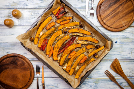 Place setting with wooden plates, rustic cutlery and baked pumpkin in baking tray on dining table. Healthy vegetarian food cooked for thanksgiving celebrationの写真素材