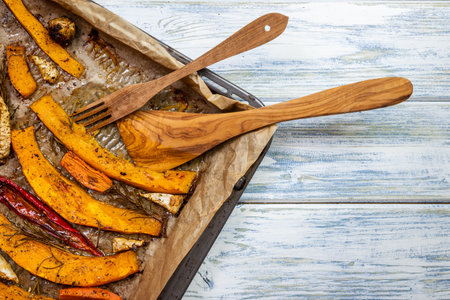 Baked pumpkin and vegetable on baking tray with rustic wooden cutlery. Serving healthy roasted food.の写真素材