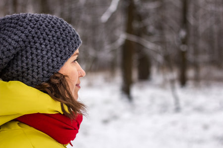 Woman with knit hat looking at snowy forest. Side view portrait of young woman wearing warm clothing in winterの写真素材
