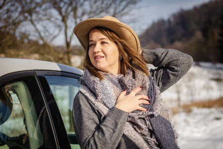 Young woman wearing cowboy hat and scarf. Traveler standing next to car during winter road tripの写真素材