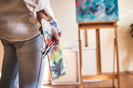 Woman painter holding palette and paintbrush and looking to her paintings on canvas. Abstract art productの写真素材