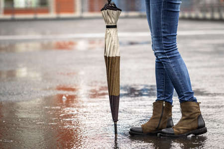 Woman with umbrella standing on city street during rain. Personal accessory and trendy casual...