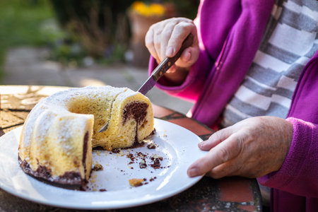 Senior woman cutting slice of bundt cake outdoors. Refreshment in spring garden. Serving Easter cake...