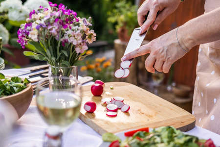 Woman chopping radish with kitchen knife on cutting board. Cooking and preparing food and vegetable...