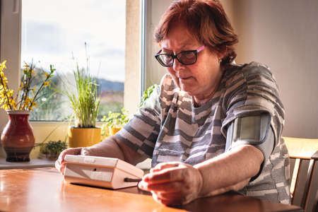 Senior woman measuring her blood pressure at home. Everyday life for hypertension patient. Diagnostic medical toolの写真素材