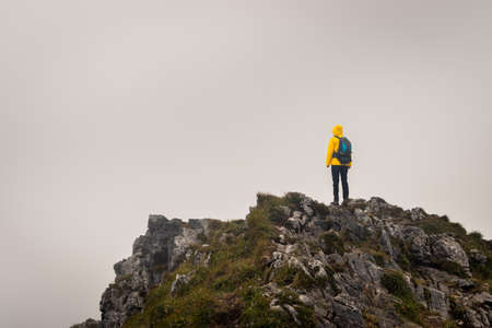 Hiker with backpack standing on the top of mountain peak. Climbing and hiking in bad weatherの写真素材