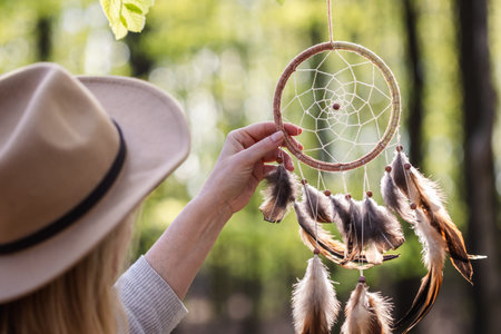 Woman with hat is hanging dreamcatcher in woodland. Indian ritual decoration. Atmospheric mood and spirituality conceptの写真素材