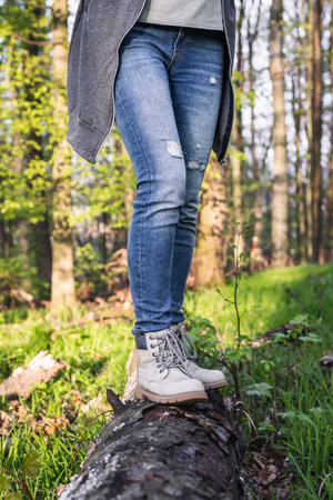 Hiking in the forest. Woman wearing jeans and standing on tree trunk at woodland. Active lifestyle in natureの写真素材