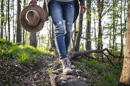 Hiking in the forest. Woman wearing jeans, holding hat and walking on tree trunk. Active lifestyle...