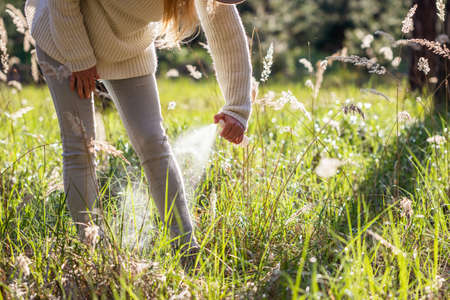Woman spraying insect repellent against tick at her legs. Protection against mosquito bite during walk in grassの写真素材