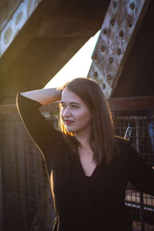 Young beautiful woman standing at bridge and enjoying sunset in city. Fashionable attractive brunette woman outdoorsの写真素材