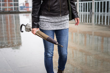 Woman holding folded umbrella and walking on city street in rain. City life and fashion accessoryの写真素材