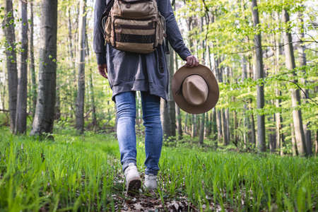 Hiking in the forest. Woman wearing jeans, holding hat and walking on footpath in woodland. Active lifestyle in natureの写真素材