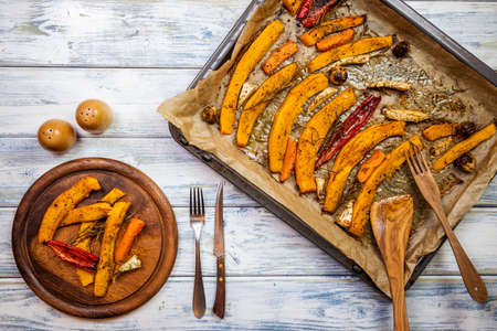 Roasted pumpkin hokkaido and vegetable on wooden plate. Baked vegetable as autumn dinner. Setting the dining table with rustic cutleryの写真素材