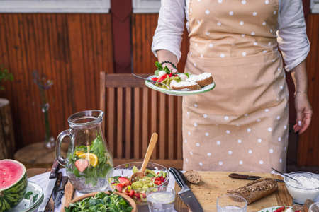 Enjoy fresh vegetable salad and baguette with cottage cheese. Woman serving vegetarian food on plate at garden party or celebration eventの写真素材