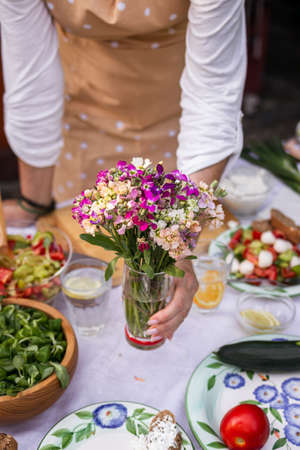Woman arranging dining table with bouquet of flowers. Setting table for garden partyの写真素材