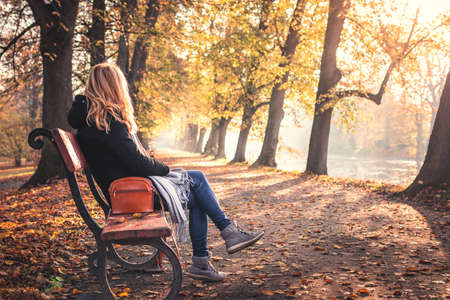 Relaxation in autumn park. Woman sitting and resting on bench in public park. Indian summer in city