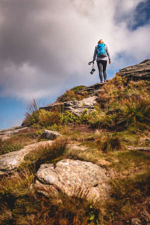 Woman with backpack and camera climbing at mountain peak. Hiking and adventure concept. Outdoors...