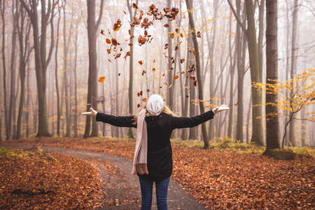 Happy woman throwing autumn leaves in the air. Enjoyment during hike in woodland at fall seasonの写真素材