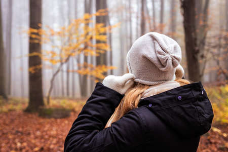 Woman pulling knit hat at her ears because freezing during hike in fall season. Warm clothing for hiking in foggy autumn forestの写真素材