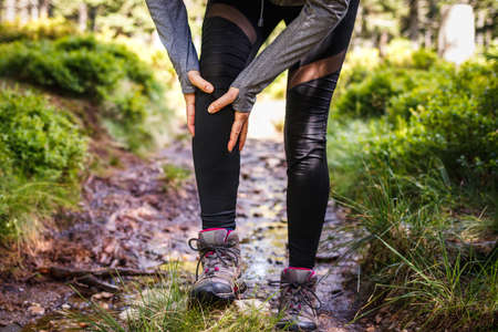 Tourist feeling knee pain. Woman injured during trek in nature. Female hiker having health problemの写真素材