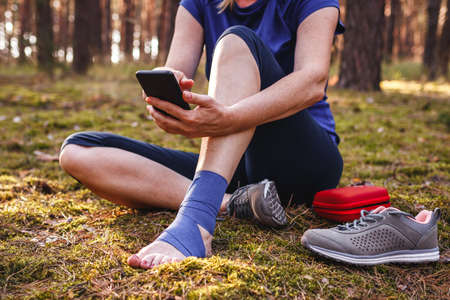 Injured hiker with sprain ankle using smart phone to get help. Woman gave herself first aid during...