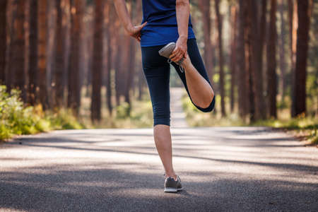 Warm up exercise before jogging. Sport training. Woman stretching before running on road in forest