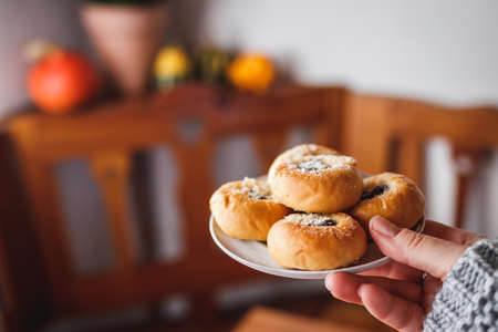 Woman holding plate with sweet baked pastry. Serving traditional homemade small sourdough buns or cakes filling with cottage cheese and jamの写真素材