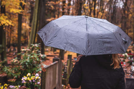 Silent grief in cemetery. Lonely sad woman mourning for dead person at graveyard. Mourner with umbrella in rainの写真素材