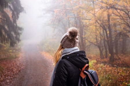 Woman with backpack and knit hat hiking in foggy forest. Tourist looking for adventure in nature. Mystery woodlandの写真素材