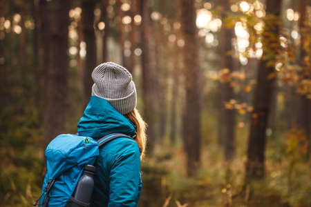 Autumn hike in forest. Woman with backpack and knit hat looking at woodland. Adventure in nature. Active lifestyleの写真素材