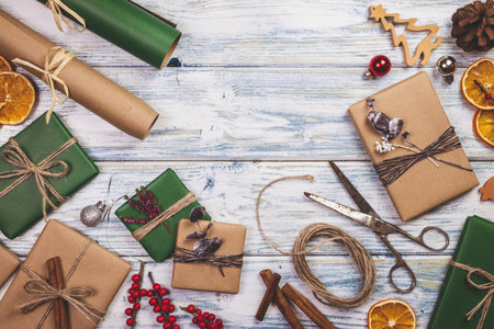 Preparing gift boxes for Christmas. Decoration and wrapped christmas presents on wooden table. Flat lay. Wrapping paper, scissors and holiday ornamentsの写真素材