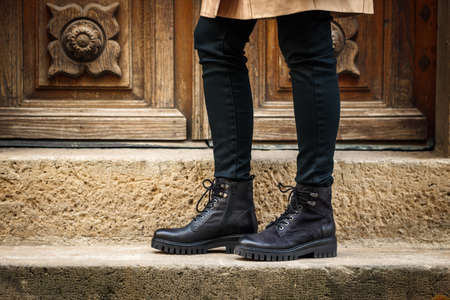 Trendy black boots. Close-up stylish leather shoes. Female legs standing on staircase on streetの写真素材