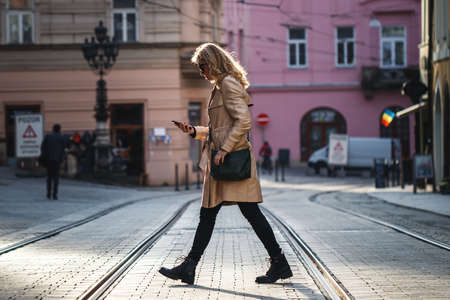 Be careful when crossing street. Woman walking in the city while reading text messages on her mobile phone. Distracted and careless people on the roadの写真素材