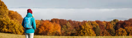 Hiking outdoors in fall season. Autumn hike in mountain forest. Woman tourist with backpack and looking at beautiful scenery. Panoramic viewの写真素材