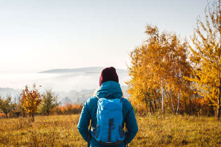 Enjoyment of autumn hike in nature. Woman tourist with backpack and knit hat looking at beautiful scenery. Hiking outdoors in fall seasonの写真素材
