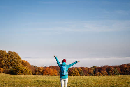 Hiking outdoors in fall season. Enjoyment of autumn hike in nature. Happy woman tourist with backpack and arms outstretched looking at beautiful sceneryの写真素材