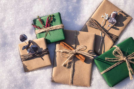 Wrapped Christmas presents with decoration in snow. Flat lay of gift boxes in green and brown kraft wrapping paperの写真素材
