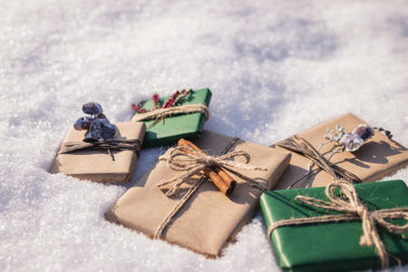 Wrapped Christmas presents with decoration in snow. Gift boxes in green and brown kraft wrapping paperの写真素材