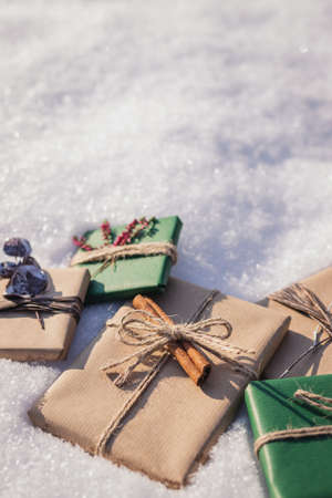 Wrapped Christmas presents with decoration in snow. Gift boxes in green and brown kraft wrapping paperの写真素材