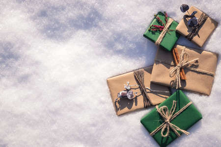 Wrapped Christmas presents with decoration in snow. Flat lay of gift boxes in green and brown kraft wrapping paperの写真素材