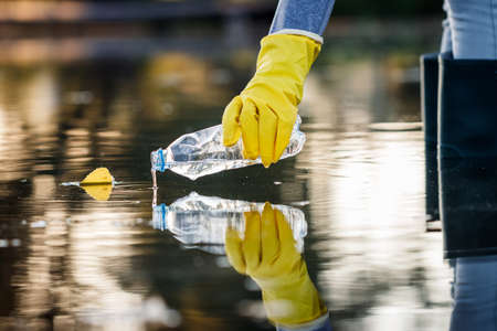 Volunteer picking up plastic bottle from polluted lake or sea. Water pollution with plastic garbage. Environmental damageの写真素材