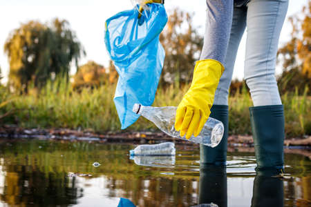 Volunteer picking up plastic bottle from polluted lake or river. Water pollution with plastic garbage. Environmental damageの写真素材
